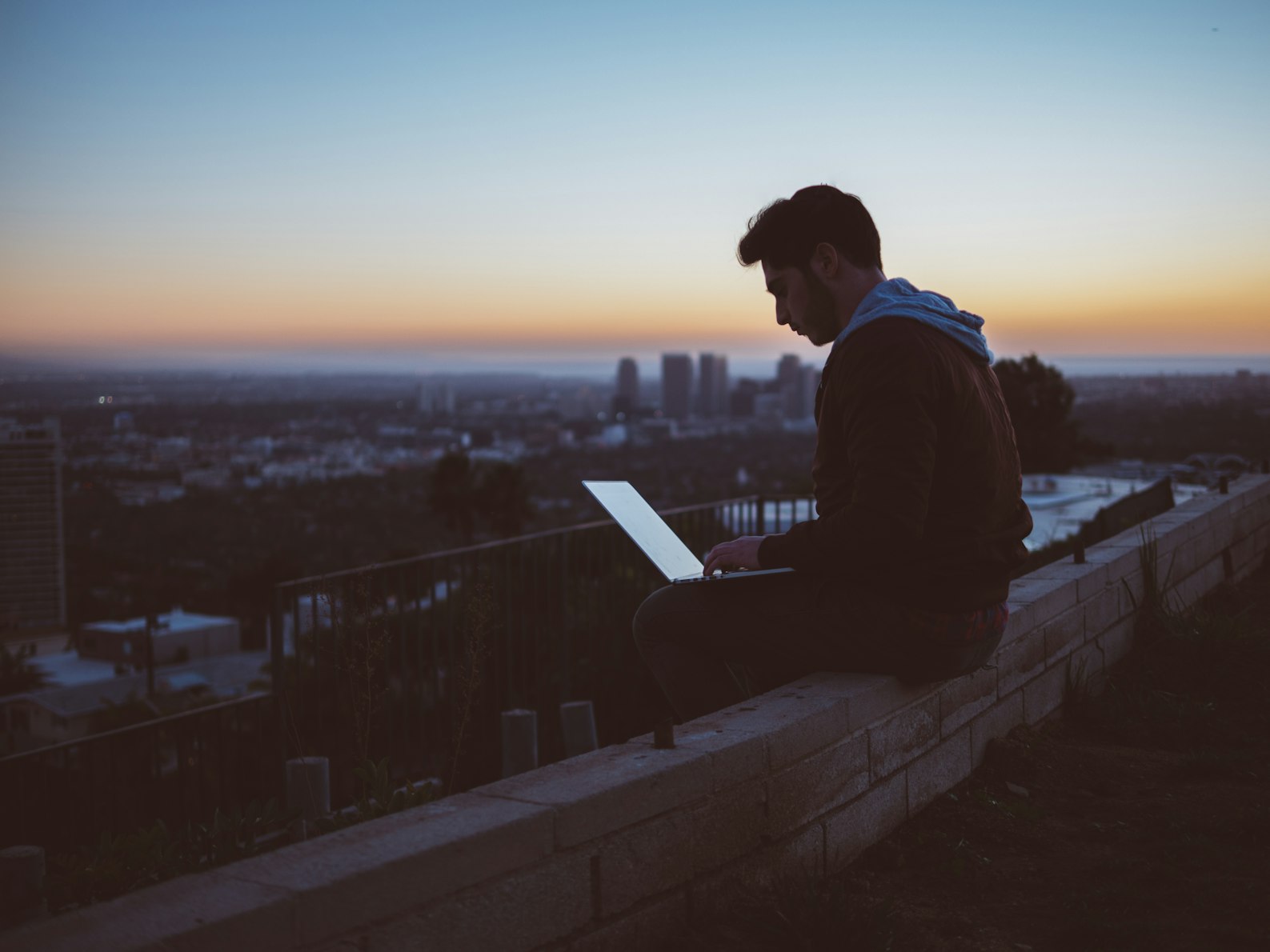 A person working on a laptop overlooking the city at sunset